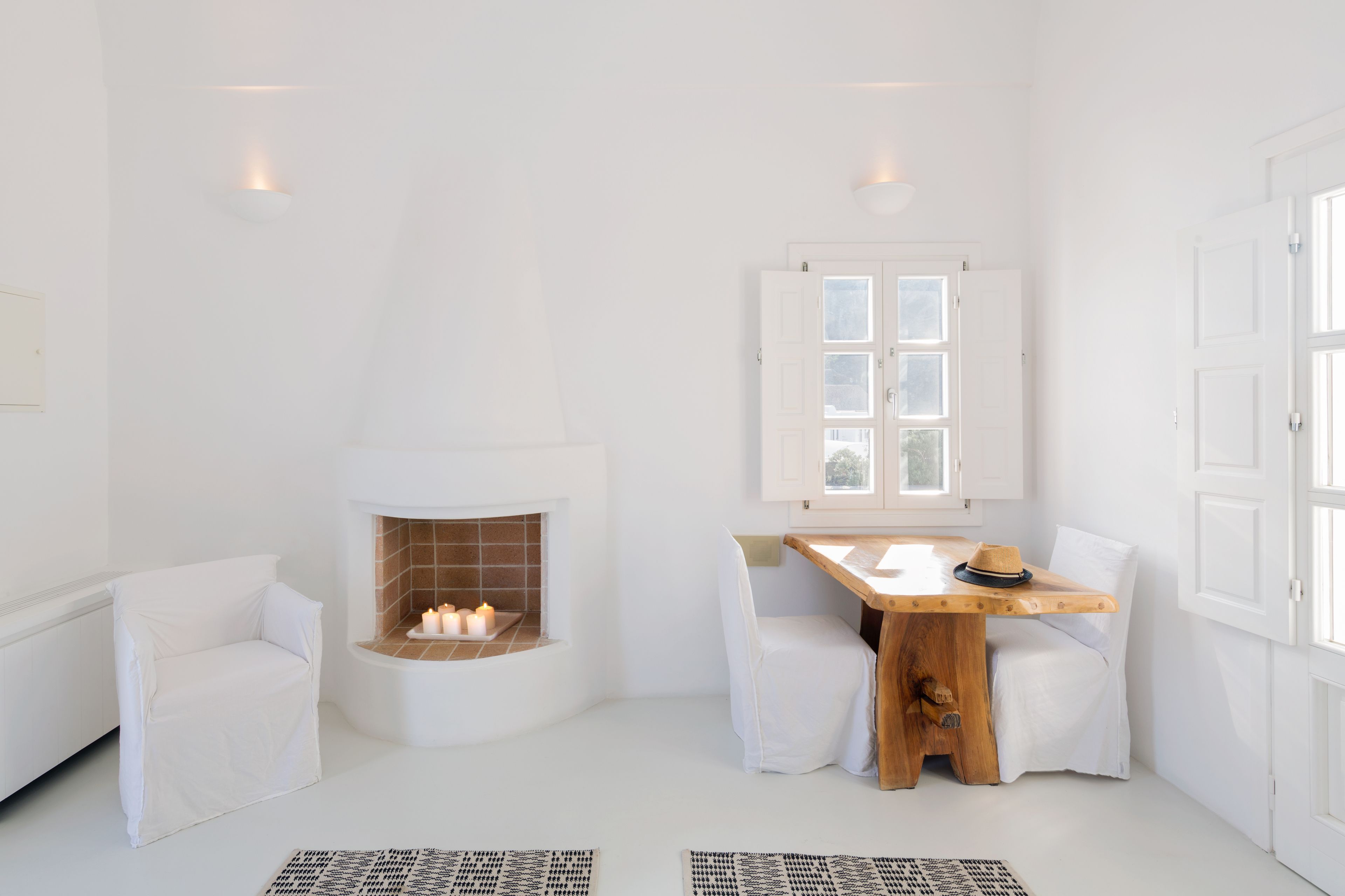 A white room with a fireplace, a table with a hat, and two chairs.