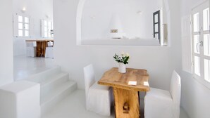 Un intérieur spacieux et lumineux, aux murs blancs, avec une table à manger en bois et des chaises blanches, un escalier menant à une autre pièce et une grande fenêtre en arc de cercle.