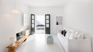 Une pièce lumineuse et blanche, avec un banc en bois, un canapé blanc et un téléviseur posé sur un meuble en bois.