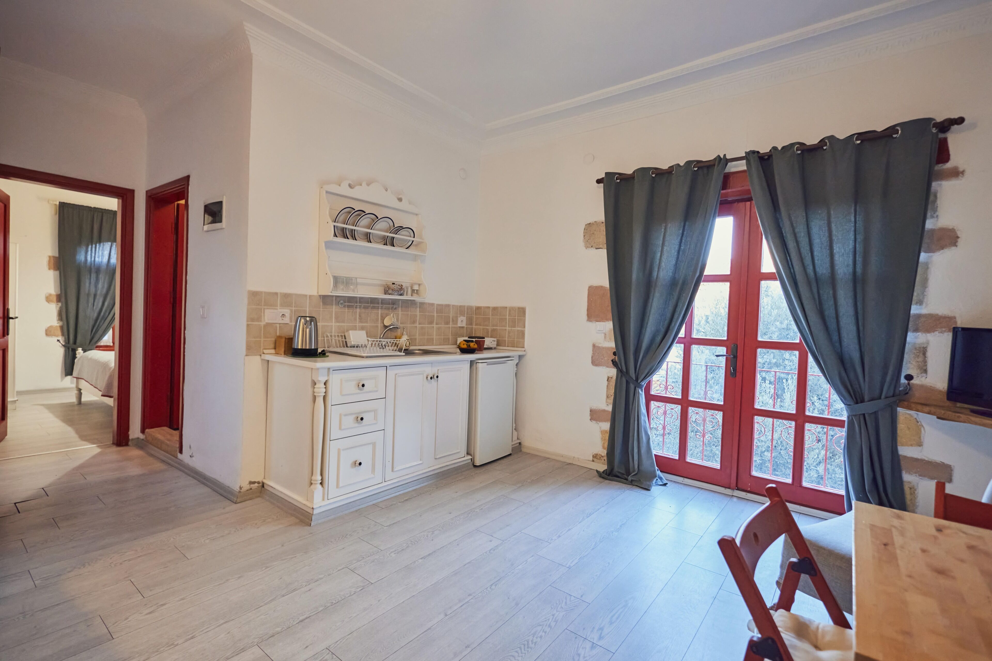 A kitchen with white cabinets, a small refrigerator, and a window with curtains.