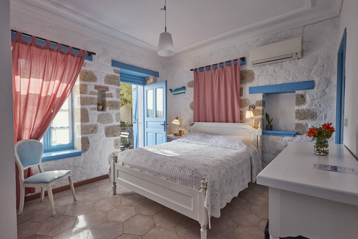 Ein Schlafzimmer mit Steinwand, einem Bett mit weißem Kopfteil, einem Sessel, einem Schreibtisch und einem Fenster mit Vorhängen.