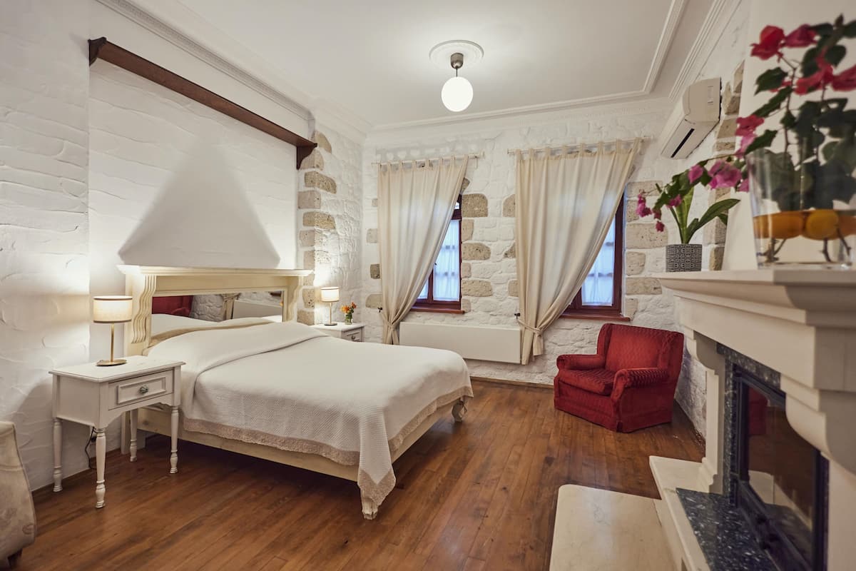 Ein Schlafzimmer mit einem großen Bett, einem roten Sessel, einem Kamin und einer Steinwand.