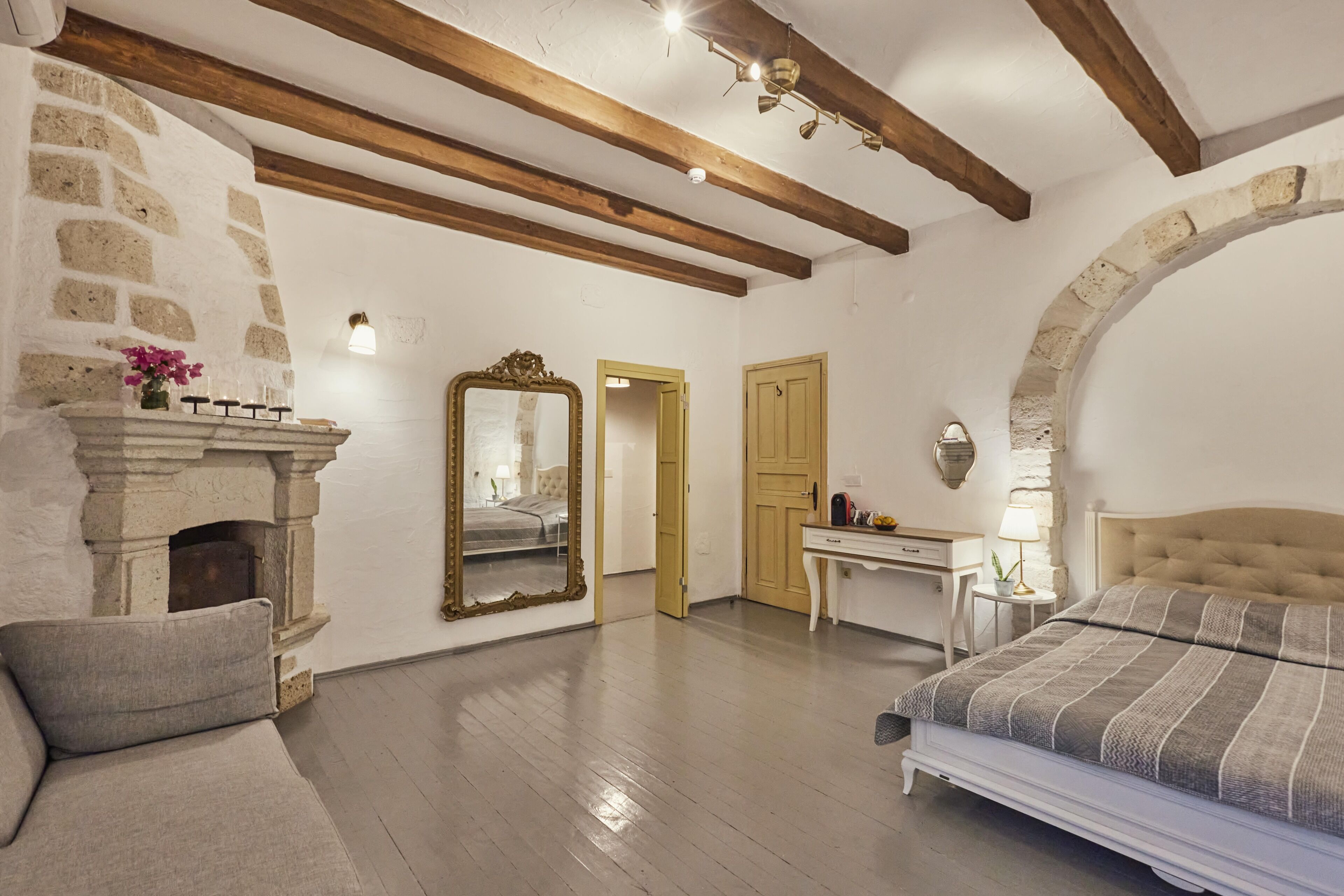 Una camera da letto con camino in pietra, travi in legno, un letto con coperta a righe, una scrivania e uno specchio.