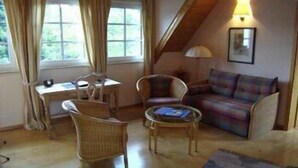 Una sala de estar acogedora con techo de madera, un sofá, dos sillones, una mesita y una ventana con cortinas.