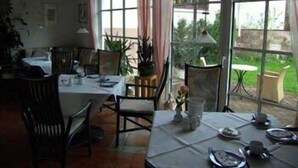 Un comedor con mesas dispuestas para comer, sillas y plantas en macetas.