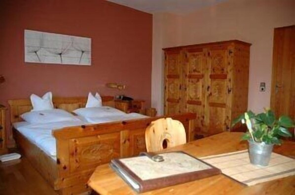 Una cama de madera con ropa blanca, un armario de madera y una mesita con una planta y un libro.