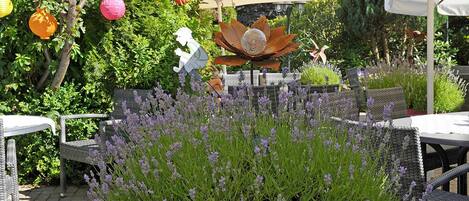 An outdoor patio area with wicker furniture, a decorative metal sculpture, and purple flowering plants.
