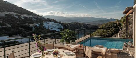 Una terraza con piscina, zona de comedor y vistas a las montañas.