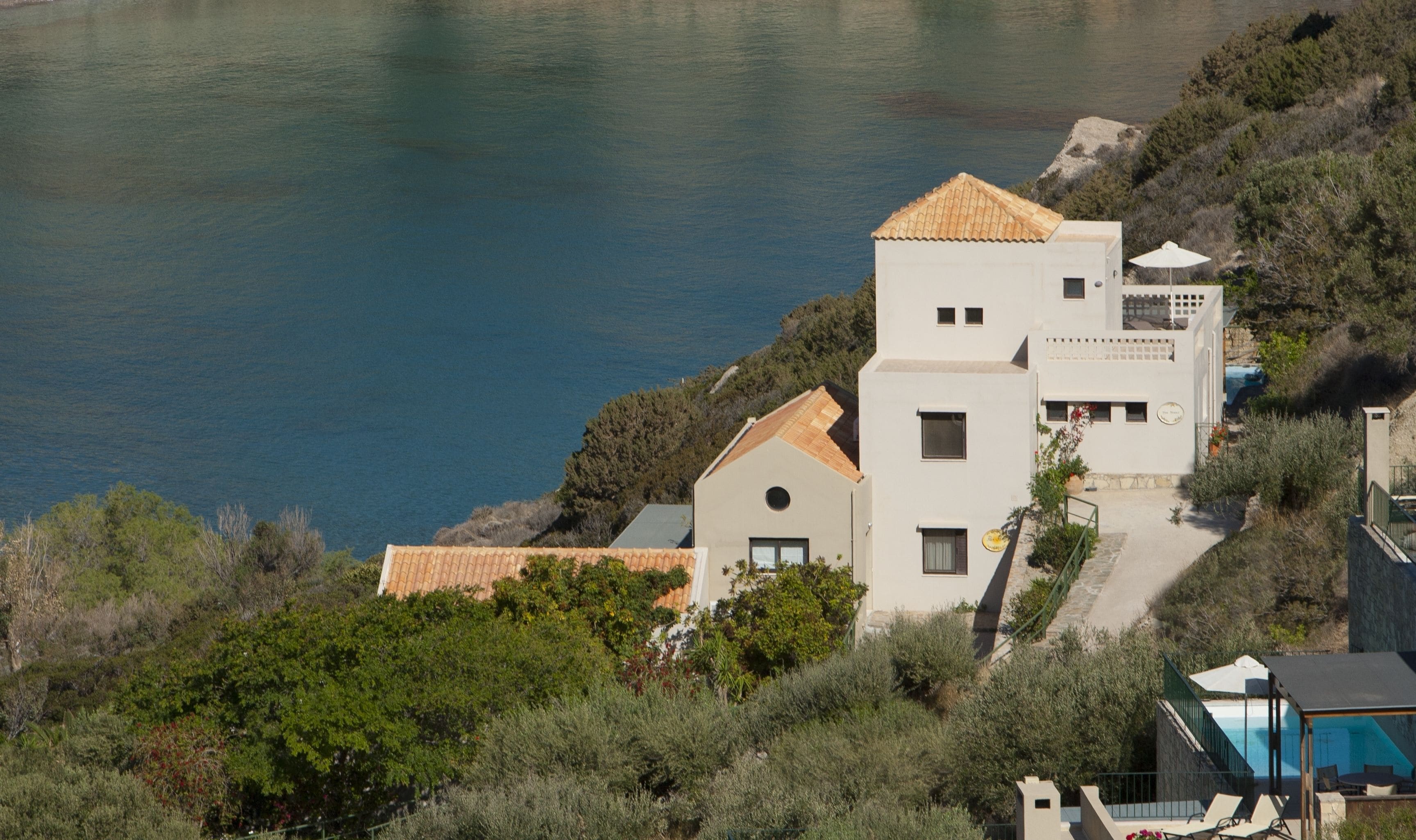 Un bâtiment situé sur la côte, doté d’une piscine, entouré de verdure et offrant une vue sur la mer.