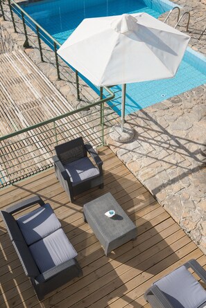 A poolside area with a wooden deck, lounge chairs, a table, and a white umbrella. - Istron Villas (Agios Nikolaos)