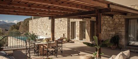 A covered patio with stone walls, outdoor furniture, and a view of mountains.