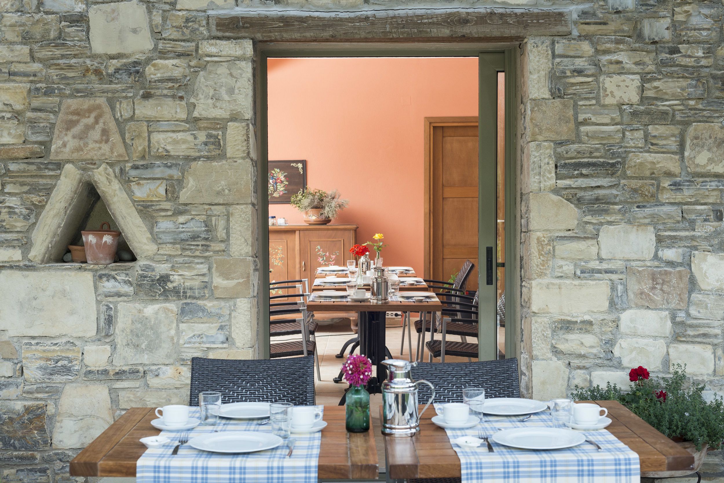 A stone-walled dining area with a wooden table set for four, surrounded by chairs.