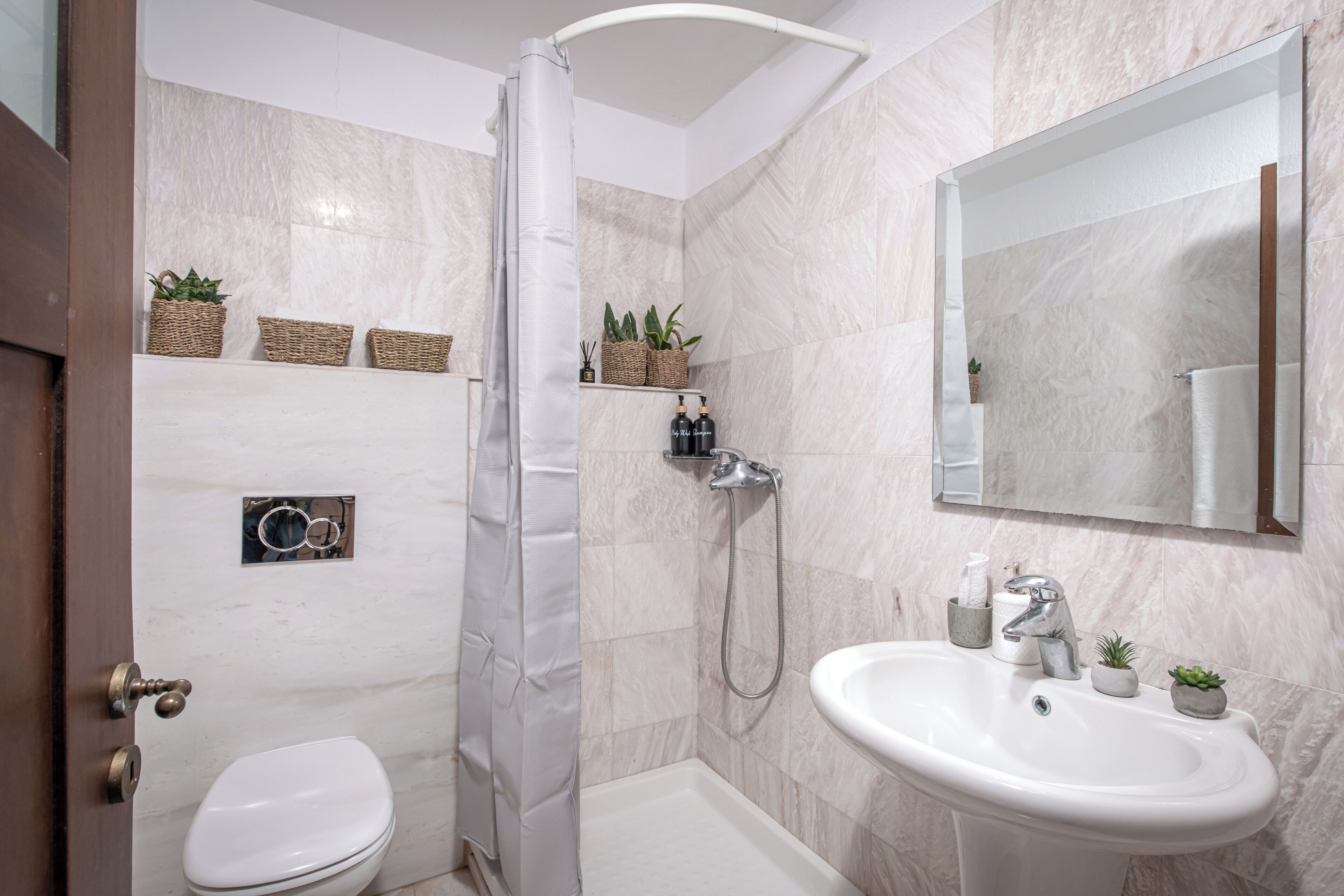 Un baño moderno con ducha, inodoro y lavabo. Hay cestos de mimbre con plantas en la pared y un espejo sobre el lavabo.