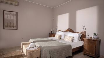 A bedroom with a large bed, two bedside tables, a nightstand, a wicker chair, and a wall-mounted air conditioner.