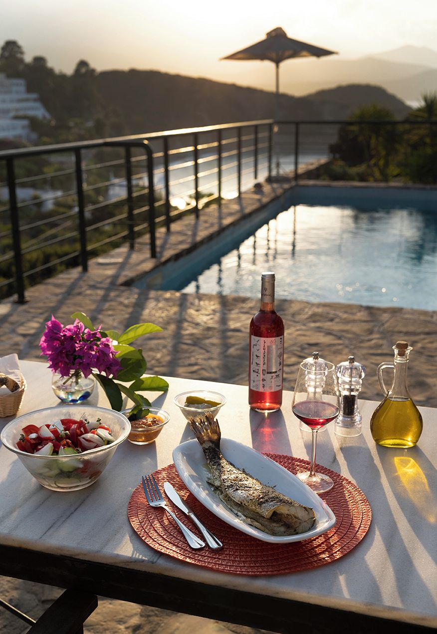A dining table with a meal, wine, and a view of a bridge over water.