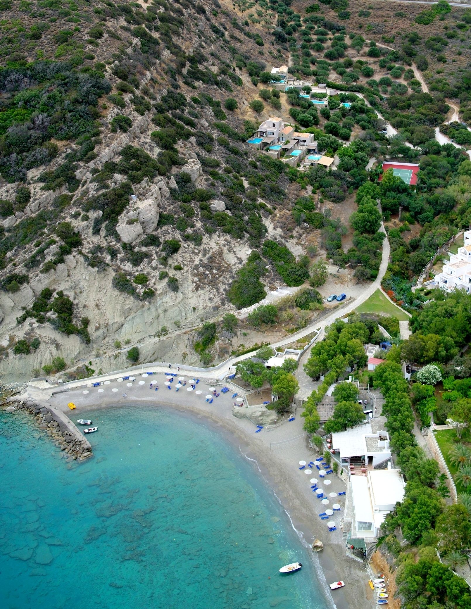An aerial view of a coastal area with a beach, a swimming pool, and several buildings.