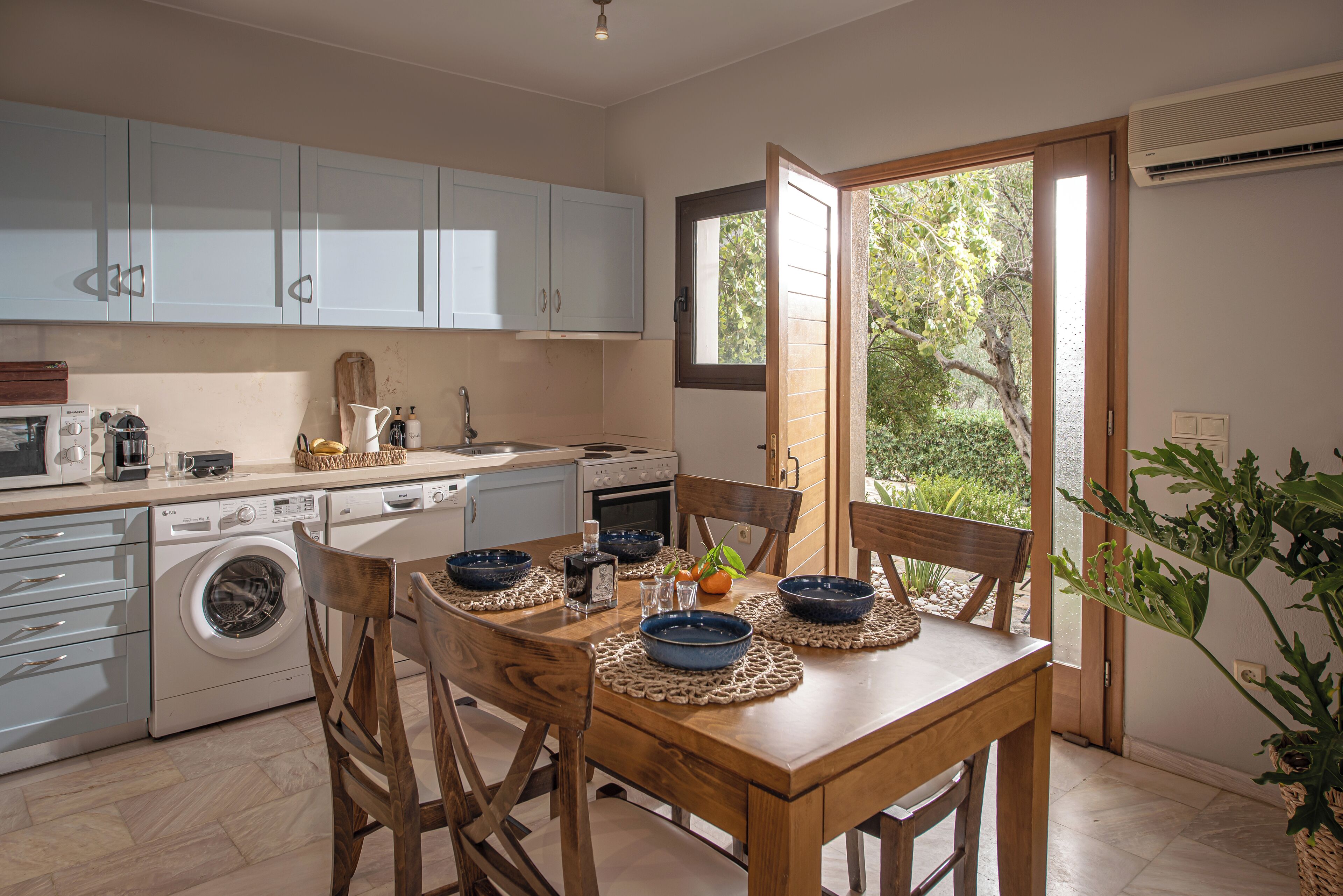 A kitchen with a dining table set for four, a washing machine, and a large window with a view of greenery.