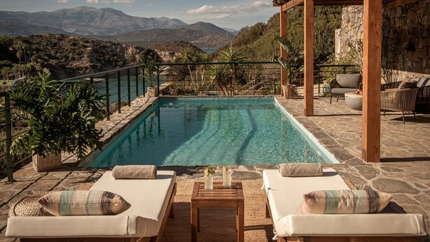 Une piscine avec vue sur les montagnes, entourée de chaises longues et d’une pergola.