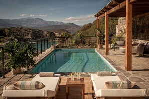 A pool with a view of mountains, surrounded by lounge chairs and a pergola. - Istron Villas (Agios Nikolaos)