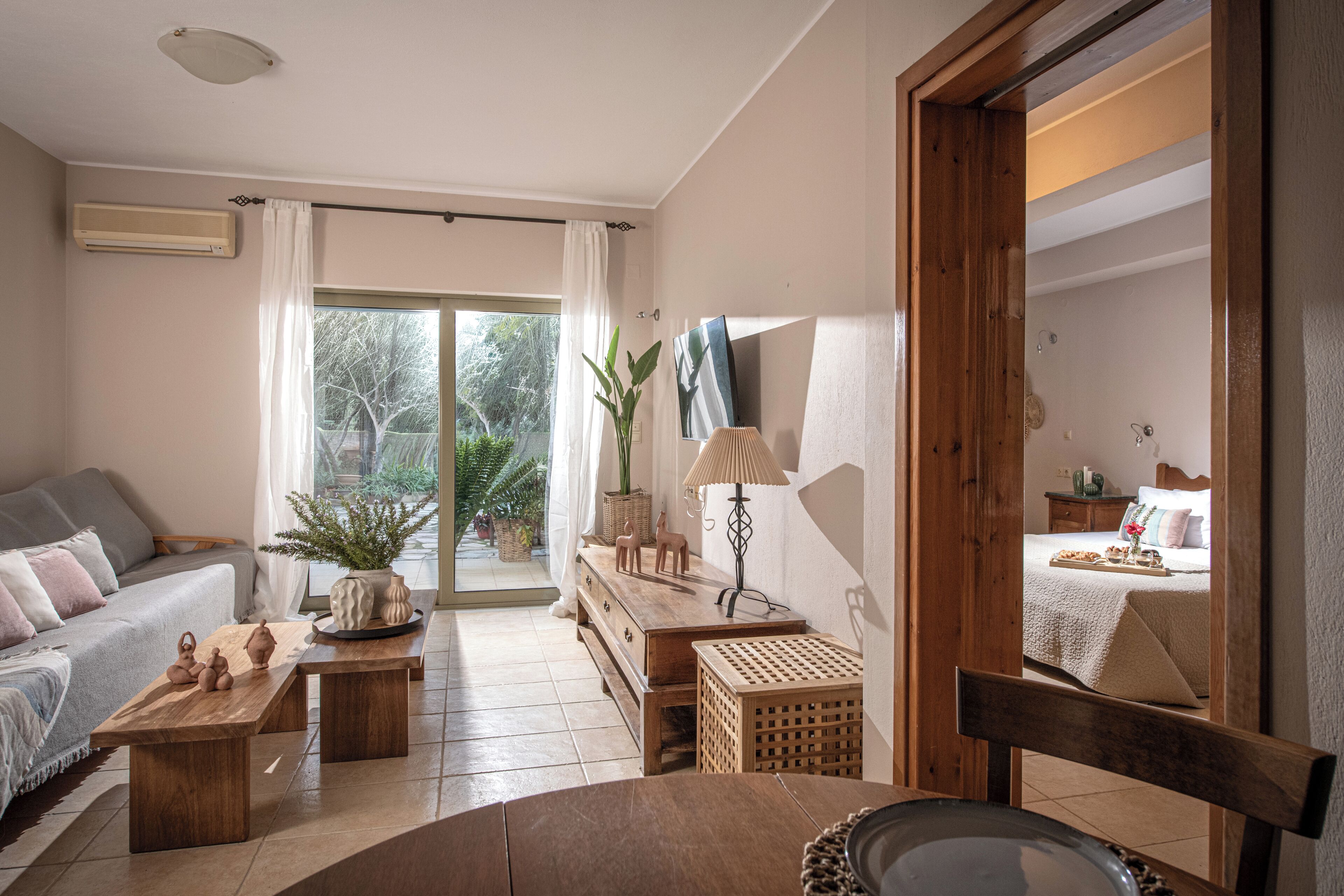 Un salon comprenant un canapé, une table basse en bois et une table à manger. On y trouve une fenêtre avec des rideaux, une plante et une lampe sur une table d’appoint en bois.