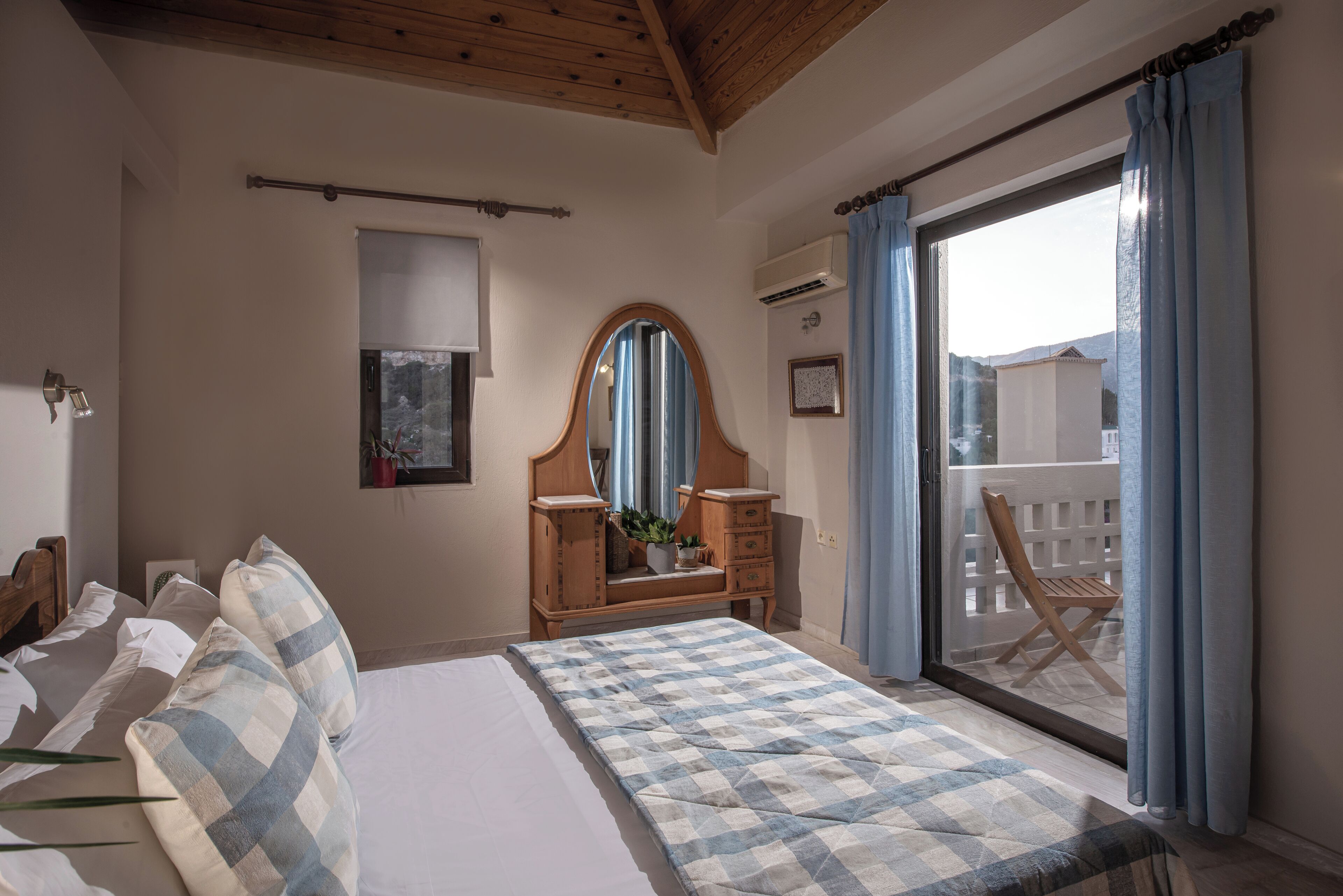 Un dormitorio con cama, cómoda de madera, espejo y balcón con una silla.