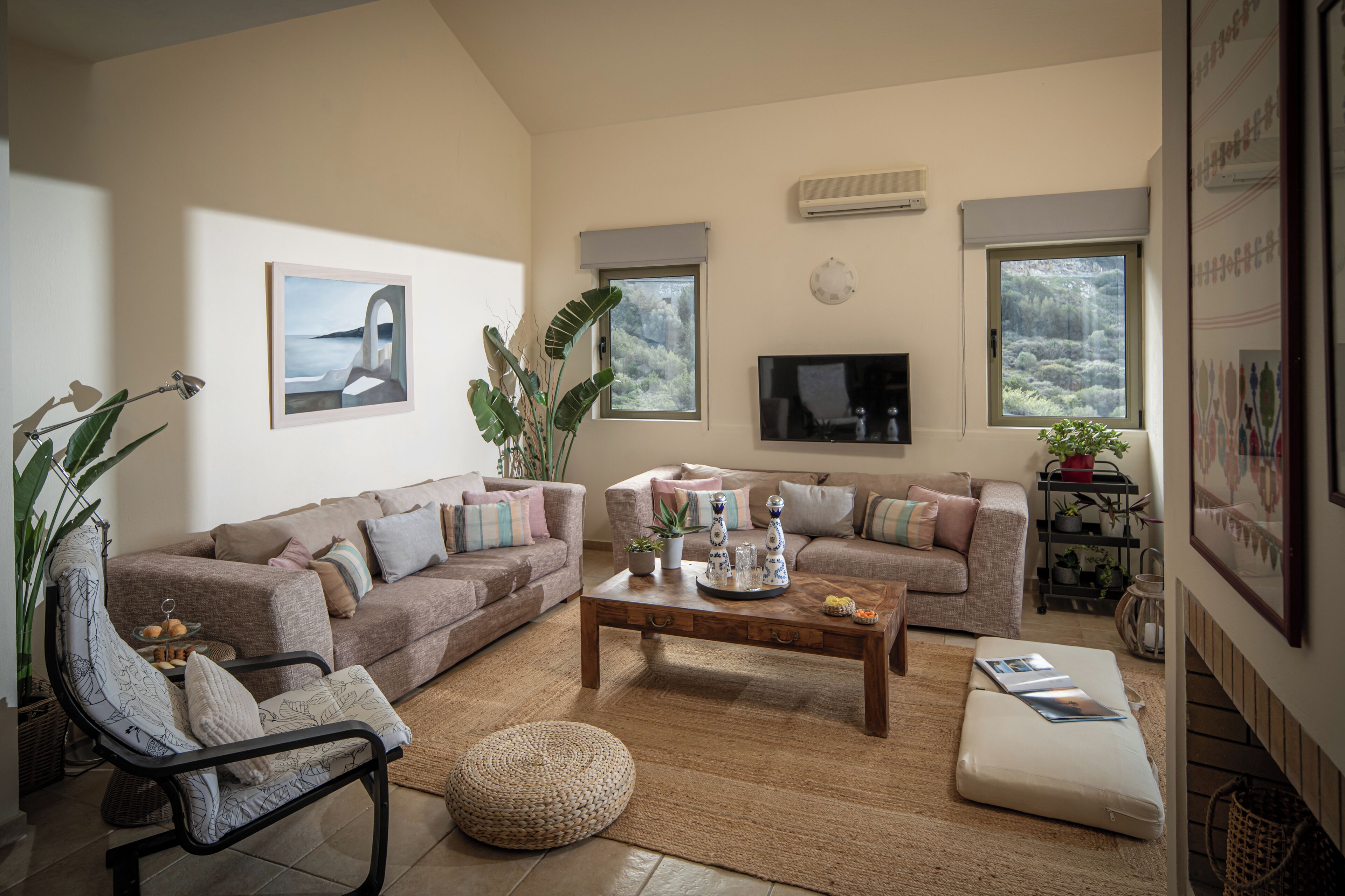 Ein Wohnzimmer mit einer Sofagarnitur, einem Couchtisch, einem Fernseher und einem großen Fenster mit Blick auf Bäume.