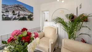 A room with a beige armchair, a large painting of a coastal village, a potted plant, and a mirror on the wall. - Lygdamis Hotel (Naxos)