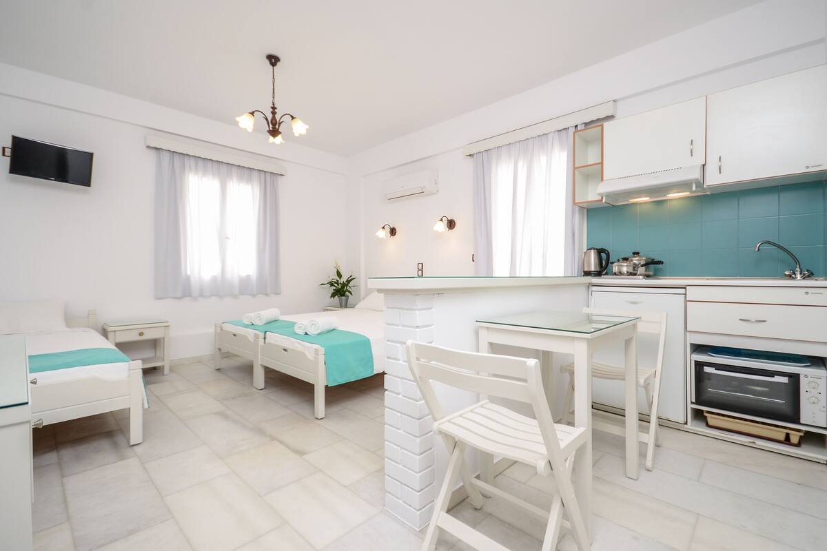 A modern, well-lit room with a bed, a desk, and a kitchenette.