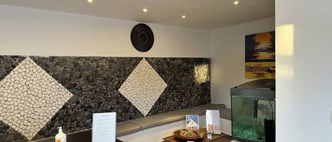 Un área de recepción con pared de mosaico de piedra, un reloj, un mostrador de recepción con una computadora, un acuario y un cuadro en la pared.