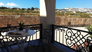 Un balcon avec un mur en pierre, une table avec un livre et une tasse, et une vue sur une ville perchée sur une colline.