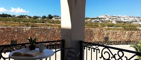 A balcony with a stone wall, a table with a book and a cup, and a view of a hillside town.
