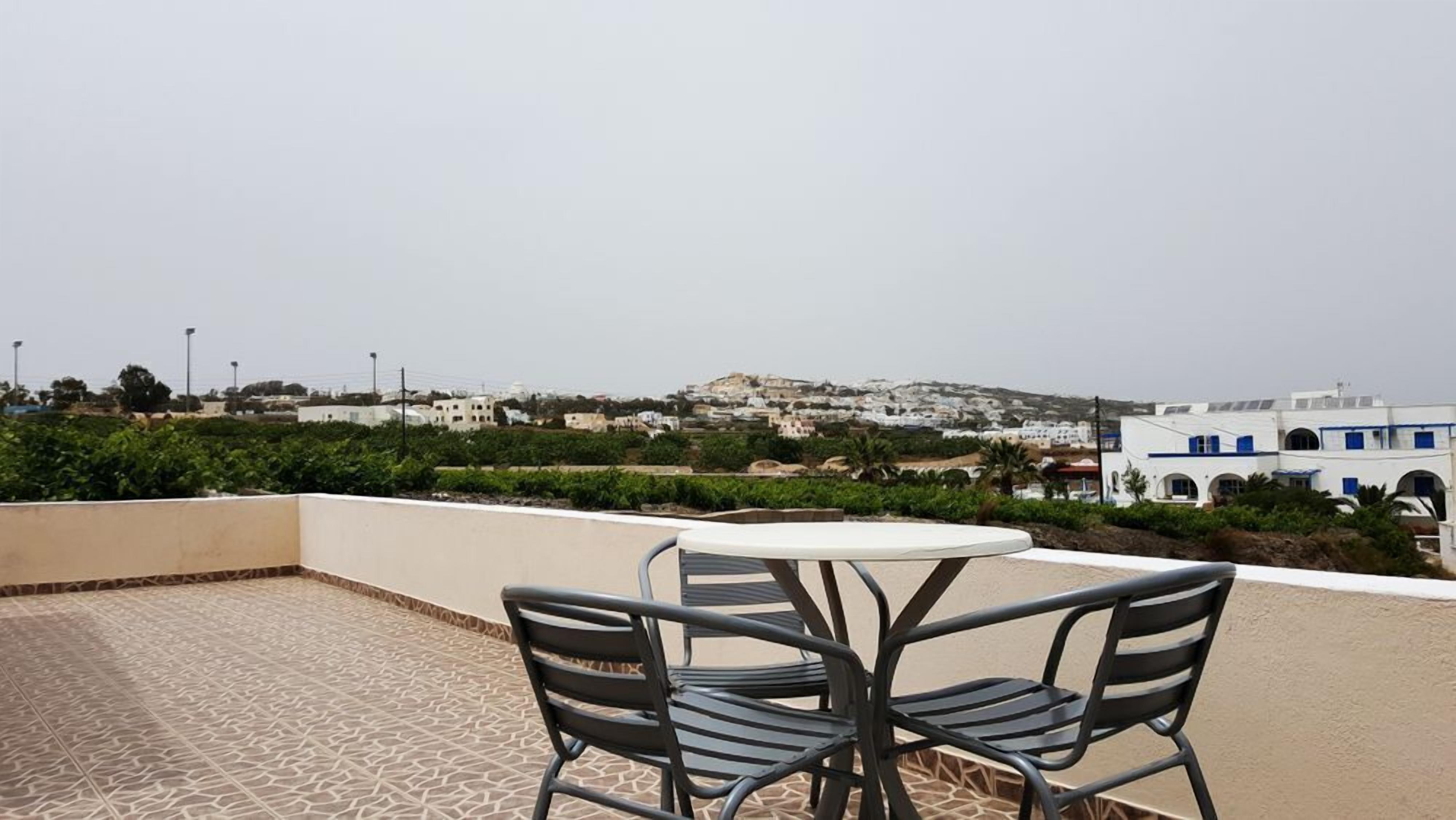 Una terraza con una mesa y sillas, con vistas a un pueblo costero de edificios blancos y un paisaje montañoso.
