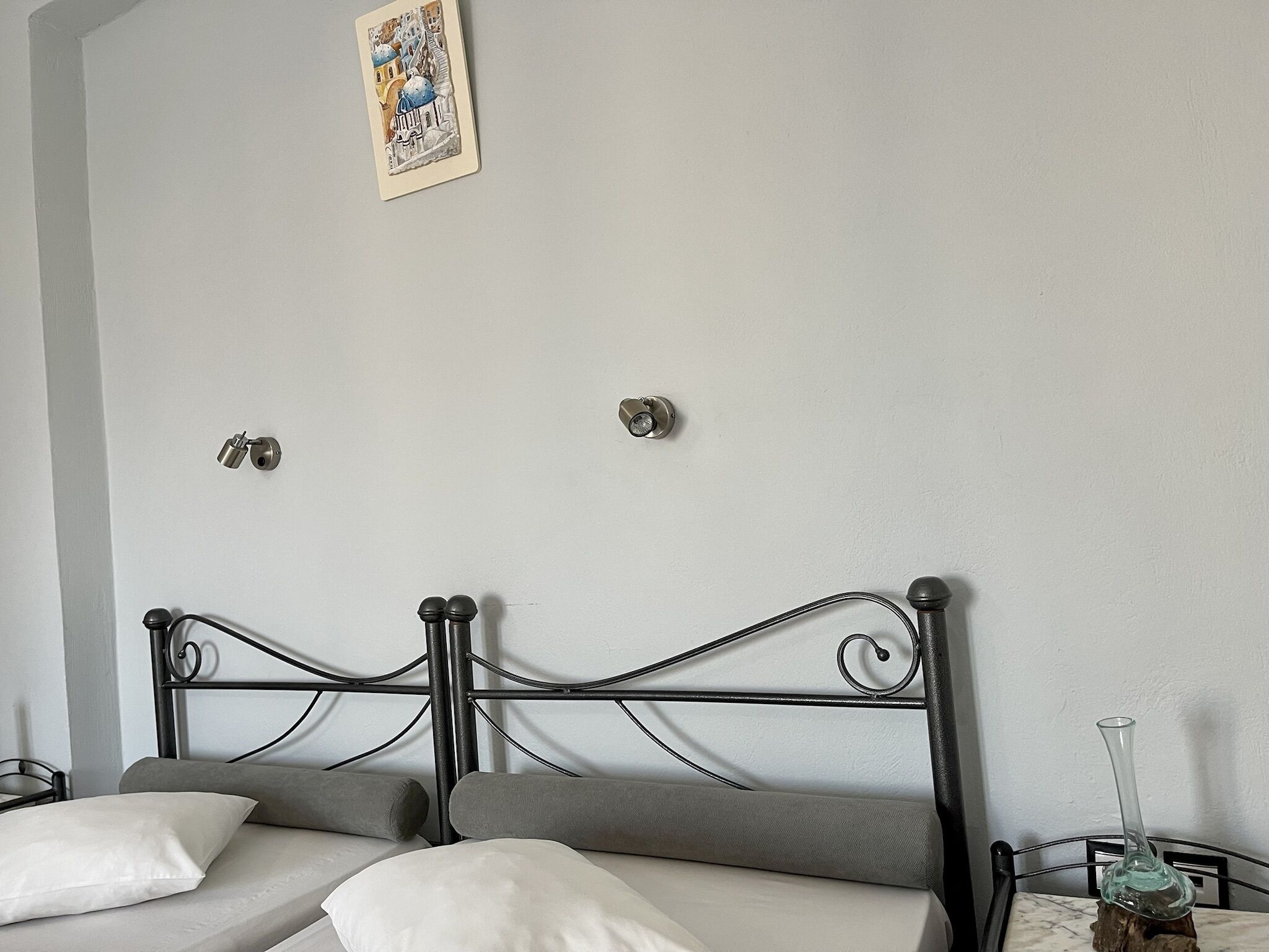 A bedroom with a bed, pillows, a nightstand, a wall clock, and a framed picture.