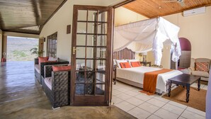 A room with a bed, a wooden table, a chair, and a window with a view of the outdoors. - Abangane Guest Lodge (Mbombela)