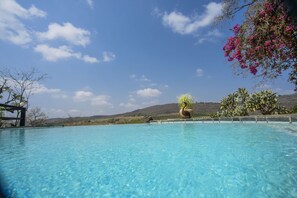Una piscina azul y cristalina con vistas a colinas y un cielo despejado.