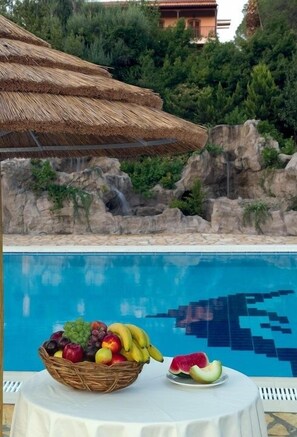 A poolside table with a fruit basket and a plate of watermelon slices. - Corfu Club (Corfu)