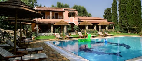 A pool area with lounge chairs, a floating pool toy, and a building with a tiled roof.