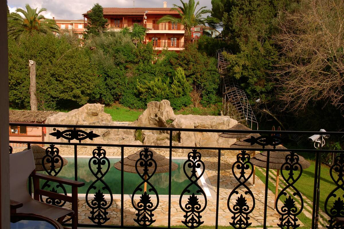 A pool with ornate black metal railings, surrounded by lush greenery and a large rock formation.