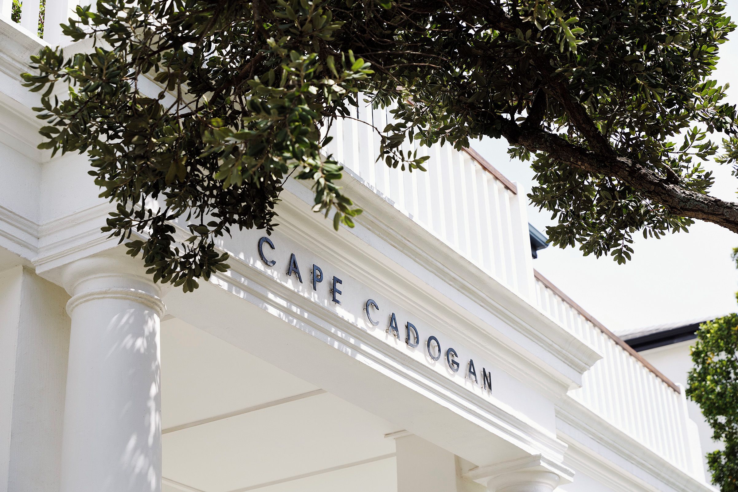 A building with the name 'CAPE CADOSAH' on its facade, surrounded by white columns and greenery.