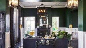Una sala de estar moderna con una pared verde oscuro, un sofá negro, una mesa de centro de vidrio y una araña.
