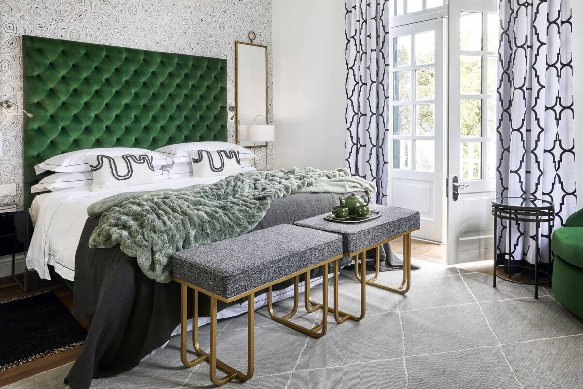 Een slaapkamer met een geborduurde groene hoofdbord, een nachtkastje met een groene plaid, en een bankje.