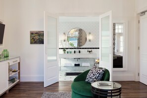 A modern living room with a green sofa, a glass coffee table, and a white tiled backsplash in the adjacent bathroom. - Cape Cadogan Boutique Hotel (Cape Town)