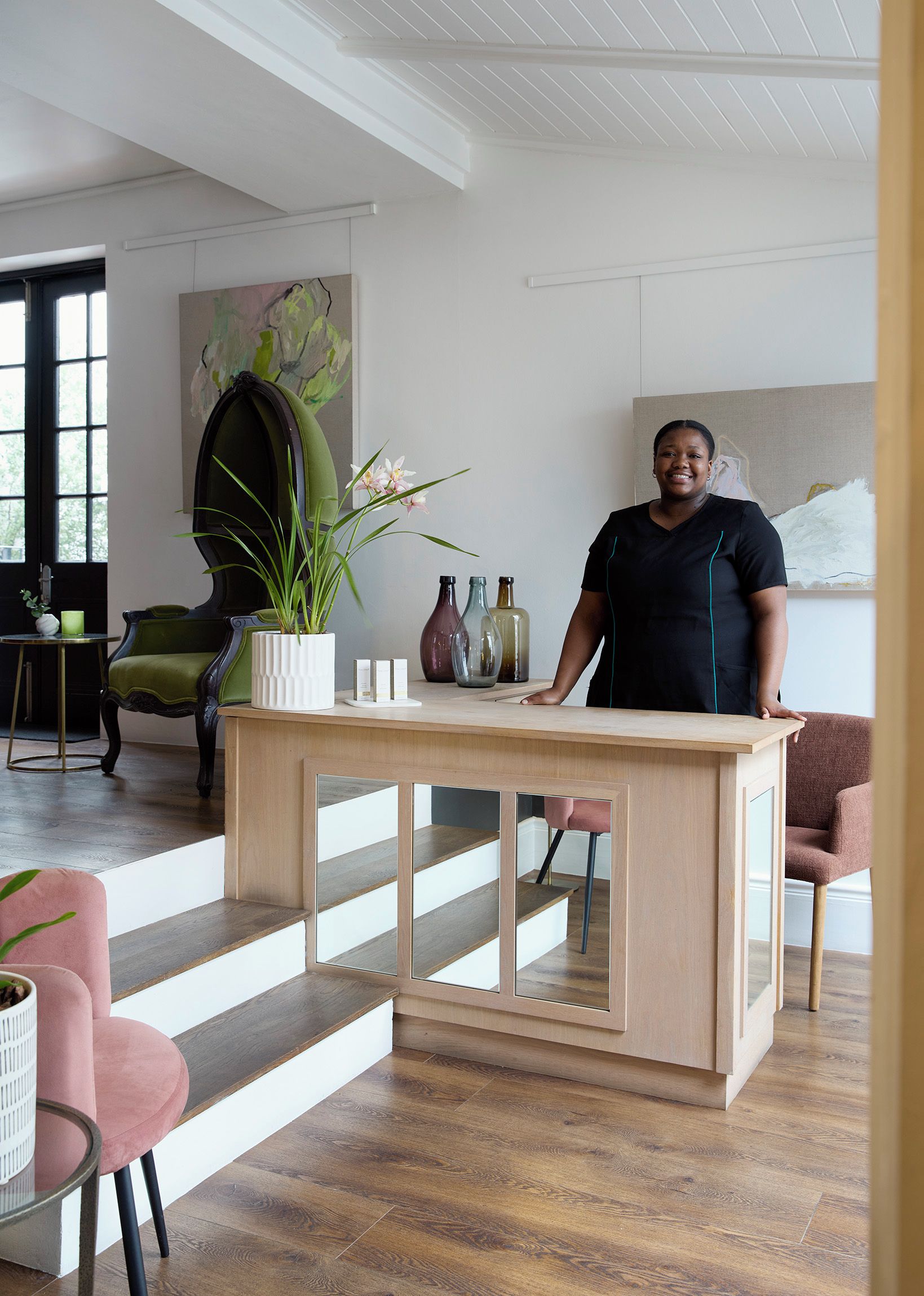 Um interior moderno com uma mesa de madeira central, uma cadeira verde e uma cadeira rosa.