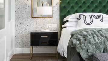 A bedroom with a green tufted headboard, a black bedside table, a gold-framed mirror, and a patterned wallpaper.