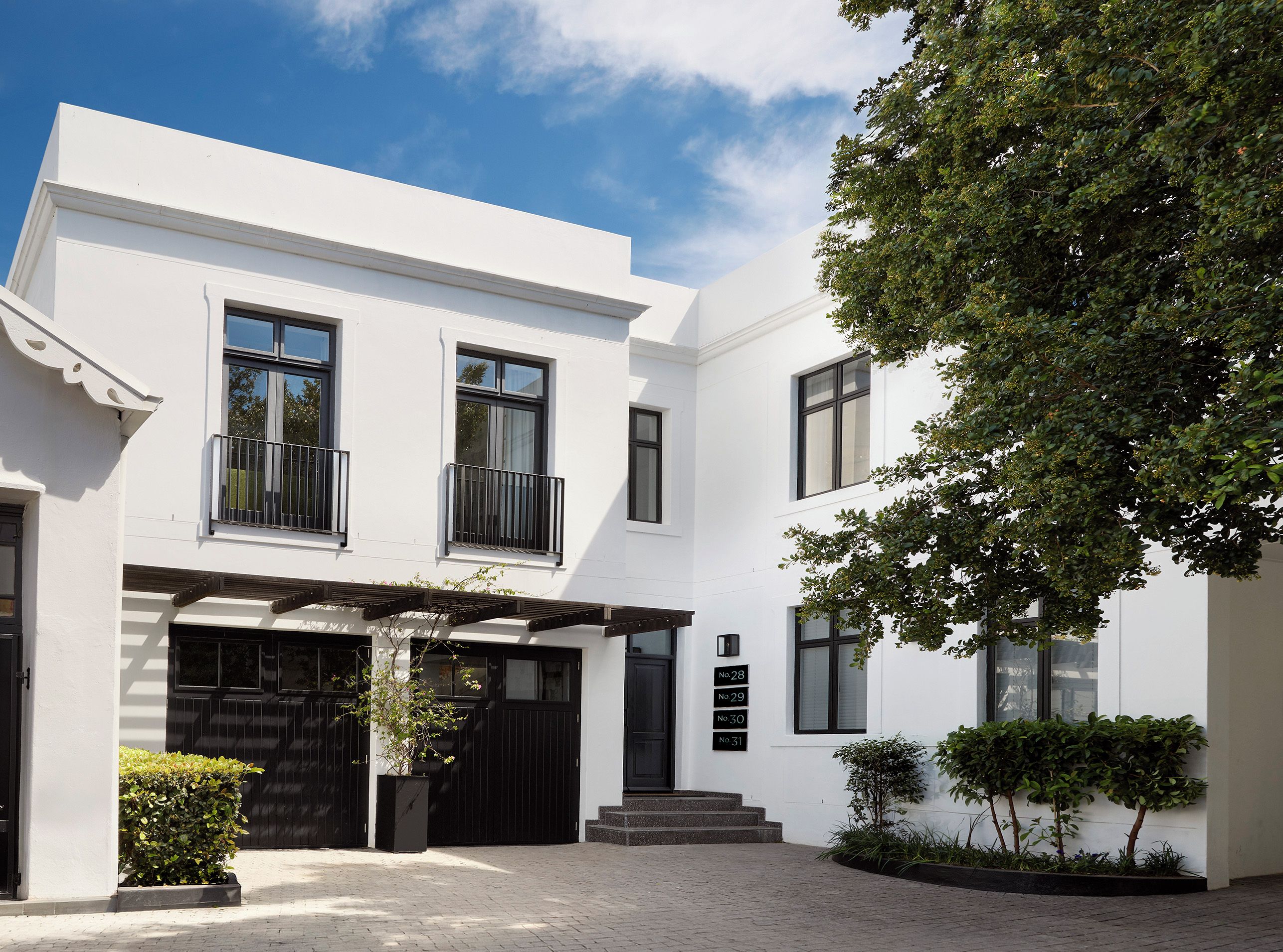 Un bâtiment moderne à deux étages, doté d’une façade blanche, de fenêtres noires et d’une porte de garage noire.