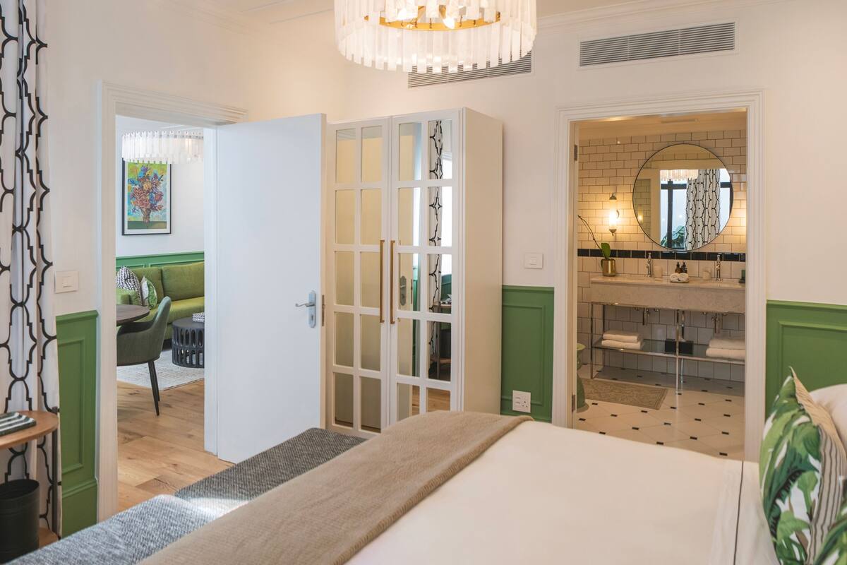 Een slaapkamer met een bed, nachtkastje, spiegel, kledingkast en een badkamer met een wastafel en spiegel.