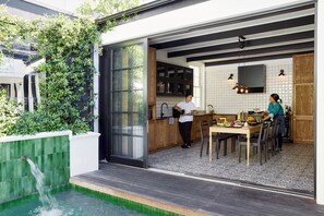 A modern kitchen with a large window, wooden cabinets, and a dining area with a table set for two. - Cape Cadogan Boutique Hotel (Cape Town)