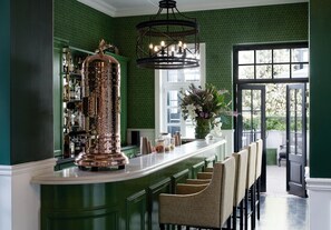 A bar area with a copper column, green patterned wallpaper, and a large window with a view. - Cape Cadogan Boutique Hotel (Cape Town)