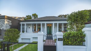 Una casa blanca con puerta verde, portón negro y cerca blanca.