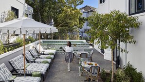 Un patio con mobiliario exterior, una persona caminando y una zona de piscina.
